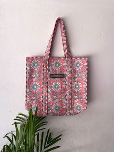 a pink and blue tote bag hanging on a wall next to a potted plant