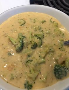 a white bowl filled with broccoli and cheese soup on top of a stove