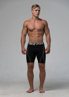 a man with no shirt standing in front of a white background wearing black trunks and shorts