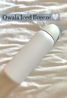 a white bottle sitting on top of a bed next to a white sheet with the words owala iced breeze