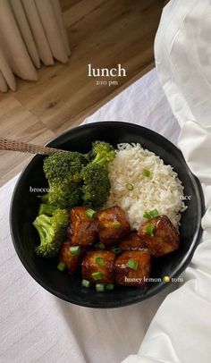 a black bowl filled with rice, broccoli and meat on top of a table