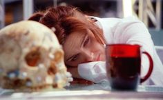 a woman laying her head on the table next to a skull