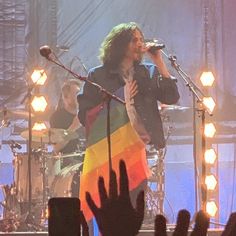 a man singing into a microphone while holding a rainbow flag in front of an audience