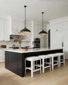 a large kitchen with white cabinets and black island in the center is surrounded by stools