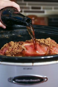 someone pouring sauce into an open crock pot filled with meat and vegetables in it