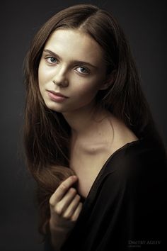 a woman with long brown hair and blue eyes posing for a photo in front of a black background