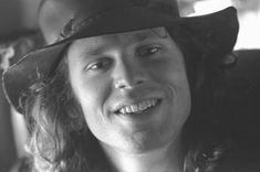 a black and white photo of a man with long hair wearing a cowboy hat smiling