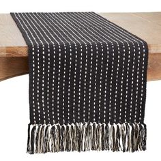 a black and white table runner with tassels on the edge, sitting on a wooden bench