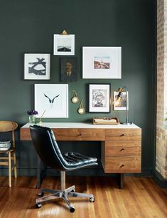 a desk with a chair and pictures on the wall above it in a room that is painted green