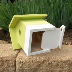 a small white and yellow birdhouse sitting on top of a stone wall next to green grass