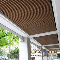 an outdoor covered porch with wood slats on the ceiling and white columns, along with trees in the background