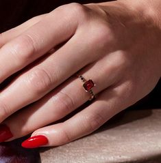 a woman's hand with red nail polish holding an apple and wearing a gold ring