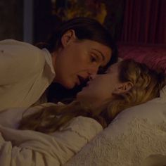 two women are laying in bed and one is kissing the other's foreheads