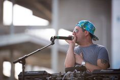 a man standing in front of a microphone with his hand on the mic and wearing a bandana