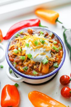 a bowl of chili with sour cream and green onions on the side next to peppers