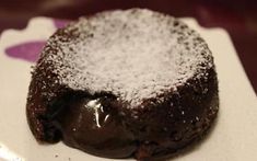 a chocolate cake with powdered sugar on top sitting on a white plate, ready to be eaten