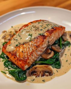 a white plate topped with salmon and mushrooms covered in gravy on top of spinach