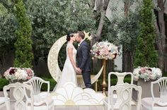 a bride and groom are standing in front of an outdoor ceremony set up with white chairs