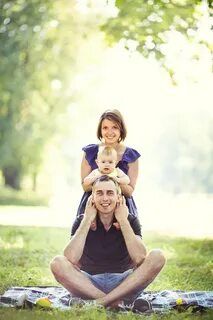 a man and woman are sitting on a blanket in the grass while holding a baby