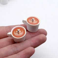 two miniature cups of coffee are sitting on someone's hand, one is white and the other is orange