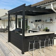 an outdoor kitchen and bar area on a wooden deck with white walls, wood flooring and black roof