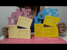 a woman sitting at a table holding up some cut out pieces of paper with the word love on them