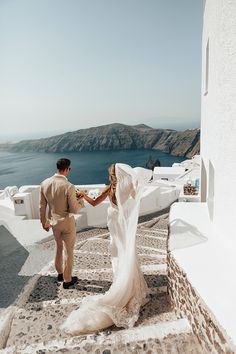 a bride and groom holding hands while walking down the stairs to their wedding venue in oia