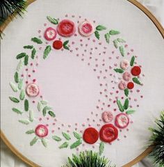 a close up of a embroidery on a white cloth with red flowers and green leaves