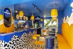 the interior of a restaurant with yellow and blue decor on the walls, tables and stools