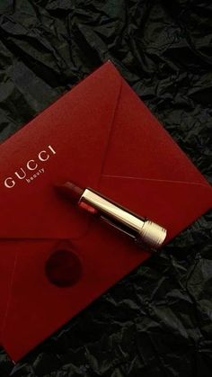 a red envelope with a lipstick on it and a gold pen laying next to it