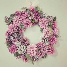 a wreath made out of pink flowers and pine cones on a white wall with a bow