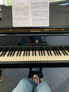 a person sitting at a piano with their feet on the keyboard and sheet music behind them