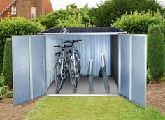 two bikes are parked in the side of a metal shed with its doors open and one bike is leaning against the wall