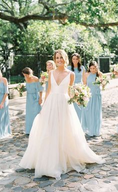 a bride and her bridesmaids in blue dresses are standing on the cobblestone