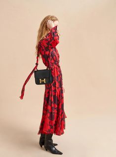 a woman in a red and black dress is holding a handbag with the letter h on it