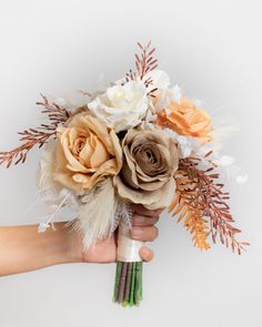 a hand holding a bouquet of flowers on a white background with leaves and twigs in the foreground