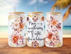 three personalized mason jars with floral designs and sayings on them, sitting on a wooden table in front of the ocean