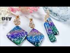 three pairs of colorful earrings sitting on top of a white table next to pink flowers