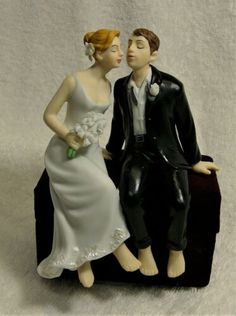 a figurine of a bride and groom sitting on a luggage bag, kissing