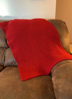 a red knitted blanket sitting on the back of a brown leather couch in a living room