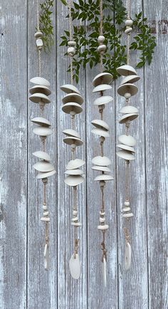 several wind chimes hanging on a wooden fence with plants growing out of one pole