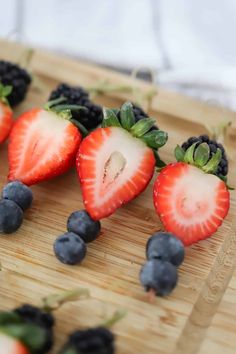 strawberries and blueberries are arranged on a bamboo cutting board, ready to be eaten