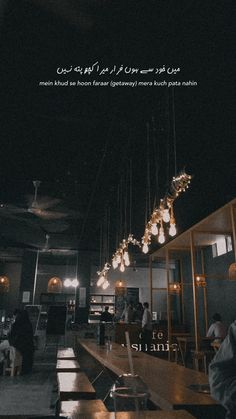 a restaurant with people sitting at tables and lights hanging from the ceiling in arabic script