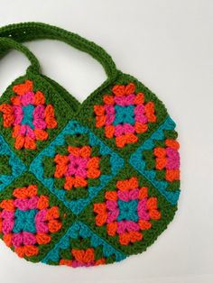 a crocheted green bag with pink, orange and blue flowers on the front