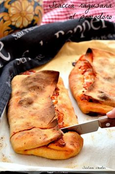 someone cutting up some pizza on top of a sheet of parchment paper with a knife