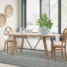 a dining table with two chairs and a vase on it in front of large windows