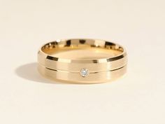 a yellow gold wedding band with a single diamond in the center, on a white background