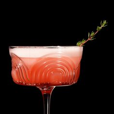 a close up of a drink in a wine glass with a sprig on the rim