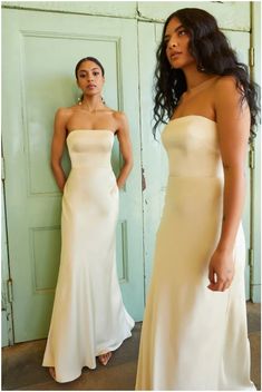 two women standing in front of a door wearing dresses and one has her hand on her hip