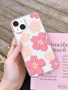 a person holding a phone case with pink flowers on it and a book in front of them